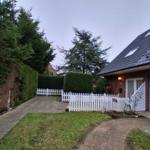 Haus mit weißen Zaun, Rasen und gepflastertem Weg. Fahrrad steht vor der Garage.