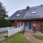 Rotes Backsteinhaus mit Dachfenstern und weißem Zaun. Eingang mit blauen Türen.