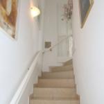 Helle Treppe mit Geländer und Wandbildern führt nach oben.