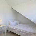 Ein Schlafzimmer mit Dachschrägen, weißem Bett und Nachttisch mit Lampe.