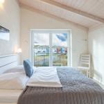 Schlafzimmer mit Bett, Fenster und Stuhl. Blick auf Außenbereich.