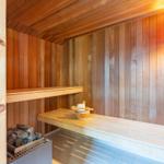Sauna mit Holzwand, Sitzbank und Körbchen mit Holzlöffel.