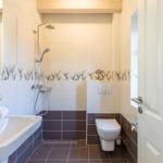 Badezimmer mit Dusche, Waschbecken und Toilette. Fliesen und Spiegel mit Fischmotiv.