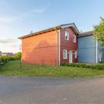 Rotes und blaues Haus mit Garten und Zaun. Hintergrund: weitere Häuser.
