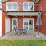 Roter Holzhaus mit Balkon, Terrasse, Tisch, Stühlen und Grill.