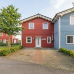Rotes und blaues Ferienhaus mit gepflastertem Vorplatz und grüner Umgebung.