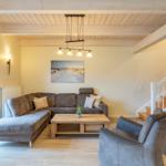 Wohnzimmer mit Sofa, Sessel und Holztisch unter Holzbalkendecke.