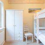 Zimmer mit Doppelstockbett, Kleiderschrank und Stuhl. Wandbild und Holzbalken.
