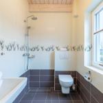 Badezimmer mit Dusche, Toilette und Waschbecken. Holzdecke und Fenster.