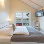 Schlafzimmer mit Bett, Fernseher und Balkontür.