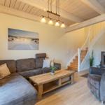 Wohnzimmer mit Sofa, Sessel, Couchtisch und Kaminofen. Holzdecke und Treppe sichtbar.