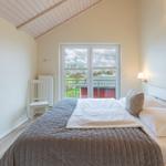 Schlafzimmer mit Bett, Fenster und Stuhl. Holzdecke und Wandbild.