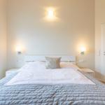 Schlafzimmer mit Bett, Nachttischen und Fenster. Weiße Wände und Beleuchtung.