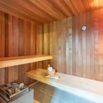 Sauna mit Holzwand, Bank, Steinkiste und Thermometer.