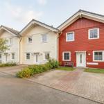 Rotes und cremefarbenes Ferienhaus mit gepflastertem Weg und grüner Umgebung.