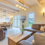 Wohn- und Essbereich mit Sofa, Sessel und Holztisch. Holzdecke und große Fenster.