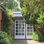 Haus mit weißen Glastüren, umgeben von grünen Sträuchern und Bäumen.