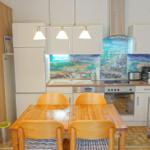 Küche mit Essbereich, Holztisch, weißen Schränken und farbigem Küchenrückwandbild.