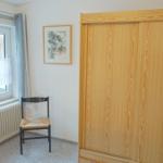Ein Zimmer mit Fenster, Stuhl und Kleiderschrank.
