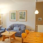 Wohn- und Essbereich mit Sofa, Tisch und Stühlen. Holzwand und Fenster sichtbar.