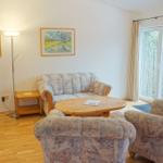 Wohnzimmer mit Sofa, zwei Sesseln, runden Tisch und Fenster zur Außenseite.