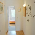 Flur mit Garderobe, Spiegel und Blick in Schlafzimmer mit Bett und Fenster.