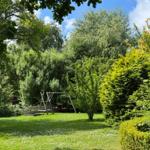 Grüner Garten mit Schaukel und Bäumen unter blauem Himmel.