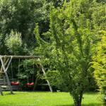Holzschaukel mit zwei roten Sitzplätzen im grünen Garten