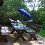 Holztisch mit Bänken, blauer Sonnenschirm und Hängemöbel im Garten.