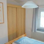 Schlafzimmer mit Bett, Schrank, Fenster und Wandbild.