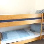 Ein Holz-Etagenbett mit blauen Bettwäsche und Kissen.