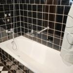 Bad mit weißem Badewannen-Set und schwarzen Fliesen an den Wänden.