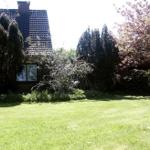 Haus mit Garten, Blumen und Bäumen im Hintergrund.