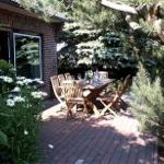 Terrasse mit Holztisch und Stühlen, umgeben von Pflanzen und Bäumen.