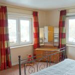 Schlafzimmer mit Bett, Kleiderschrank und Fenstern mit Vorhängen.