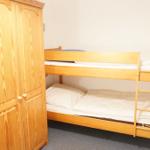 Zimmer mit Doppelstockbett und Holzschrank. Bettwäsche weiß.