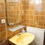 Badezimmer mit gelbem Waschbecken, Spiegel und Heizkörper an braunen Fliesenwänden.