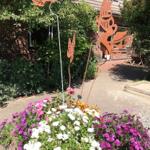Garten mit Blumenbeete und Metallfiguren vor einem Haus.