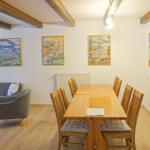 Wohn- und Essbereich mit Holzdecke, Sofa, Tisch und Wandgemälden.