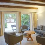 Wohnzimmer mit Sofa, Stühlen, Fernseher und Blick auf Garten.