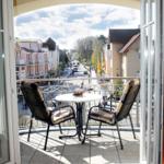 Balkon mit Tisch und zwei Stühlen. Blick auf eine Straße mit Gebäuden.