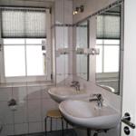 Badezimmer mit zwei Waschbecken, Spiegel und Fenster mit Rollladen.