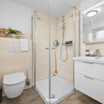 Badezimmer mit Dusche, Waschbecken und Toilette. Beleuchteter Spiegel und Handtuchhalter.