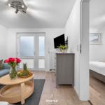 Wohnbereich mit Sofa, Couchtisch und Fernseher. Nebenraum mit Bett und Fenster.