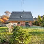 Ein Haus mit Garten, Terrasse und Gartenmöbeln unter klarem Himmel.