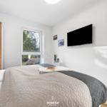 Schlafzimmer mit Bett, Fernseher und Fenster mit Blick auf Grün.