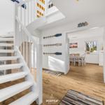 Haus mit weißer Treppe und Holzboden. Im Hintergrund ist Essbereich mit Tisch und Stühlen.