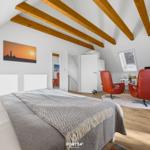 Schlafzimmer mit Dachschrägen, Bett, roten Sesseln und TV.