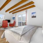 Schlafzimmer mit Dachschrägen, Holzbalken, Bett, zwei roten Sesseln und Fenstern.