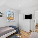 Zimmer mit zwei Betten, Fenster und TV-Schrank. Blick auf Dachziegel.